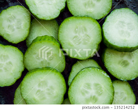 Bunch of sliced fresh green cucumbers on the black background, top view of cucumber slices in the bowl covered with water drops. 135214252