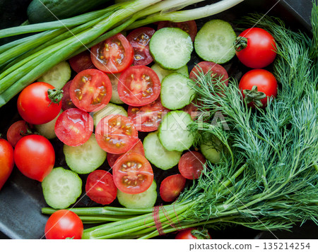 Fresh red cherry tomatoes, green leek, radish and cucumber in pan on black background, top view of vegetables covered with water drops. 135214254