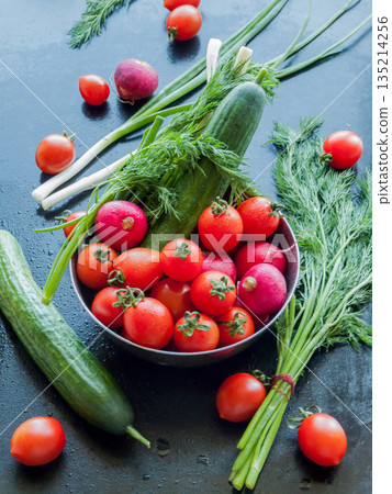 Bowl of fresh red cherry tomatoes, herbs, cucumber and radish on table background, close up vegetables in bowl covered with water drops. 135214256