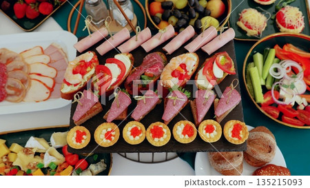 Gourmet appetizers and canapes arranged elegantly on white draped table, representing professional catering service for upscale event Gourmet appetizers and canapes arranged elegantly on white draped table, representing professional catering service for upscale event 135215093