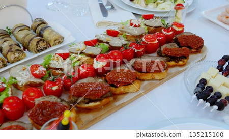 Wooden platter displaying gourmet appetizers, stuffed cherry tomatoes, sun dried tomato bruschetta, pate crostini, complemented by assorted small bites at elegant catered gathering 135215100