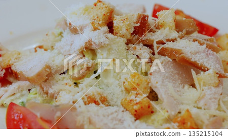Caesar salad presenting grilled chicken, crispy croutons, grated parmesan, fresh tomato wedges arranged on pristine white plate, capturing appetizing culinary detail 135215104