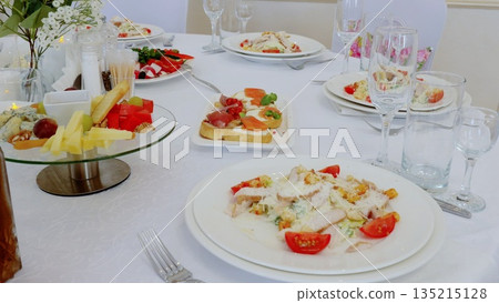 Gourmet caesar salad adorning white tablecloth, complemented by refined appetizers and crystal glassware, evoking upscale dining ambiance 135215128