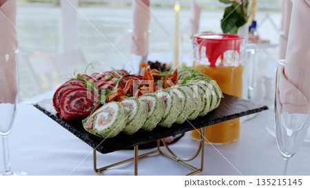 Gourmet catering display featuring spinach, beet, cream cheese rolls with shrimp on slate plate, paired with champagne and orange juice Gourmet catering display featuring spinach, beet, cream cheese rolls with shrimp on slate plate, paired with champagne and orange juice 135215145