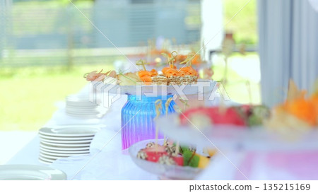 Gourmet catering display featuring salmon, cheese canapes elegantly presented on tiered stands with stacked plates at refined outdoor dining event 135215169