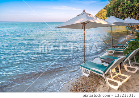 Beach chairs and umbrellas lined up on a serene tropical beach with crystal clear blue water 135215313