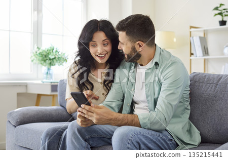 Happy couple using smartphone to celebrate good news, woman pointing to screen Happy couple using smartphone to celebrate good news, woman pointing to screen 135215441