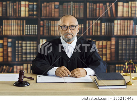 Judge in robe sitting at brown desk with gavel and balance scales, law books 135215442