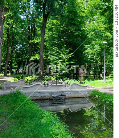 Decorative white stone bridge over a calm pond in a green city park Decorative white stone bridge over a calm pond in a green city park 135216484
