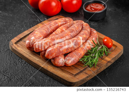Raw sausages with rosemary and tomatoes on wooden cutting board over dark background Raw sausages with rosemary and tomatoes on wooden cutting board over dark background 135216743