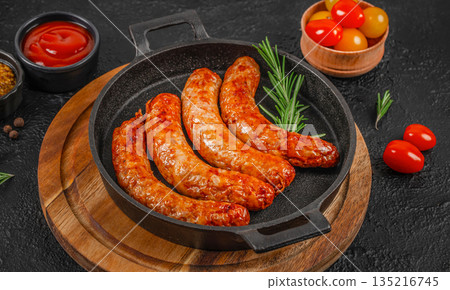 Grilled sausages in cast iron pan with rosemary and cherry tomatoes on dark background Grilled sausages in cast iron pan with rosemary and cherry tomatoes on dark background 135216745