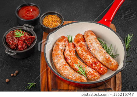 Grilled sausages in red skillet pan with sauces on dark rustic background 135216747