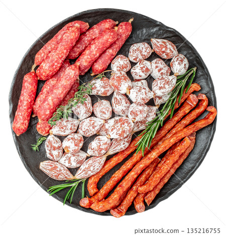 Assorted cured sausages with herbs on black stone plate isolated on white background, top view Assorted cured sausages with herbs on black stone plate isolated on white background, top view 135216755