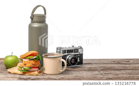 Outdoor travel lunch with sandwich, coffee mug, reusable water bottle and vintage camera on wooden table isolated on white background with copy space 135216778