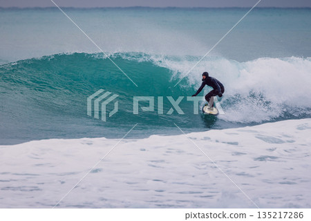 Surfer in wetsuit rides on wave in ocean. Winter surfing on perfect waves Surfer in wetsuit rides on wave in ocean. Winter surfing on perfect waves 135217286