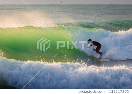 Surfer male ride on wave in cold winter ocean with evening sun light Surfer male ride on wave in cold winter ocean with evening sun light 135217295