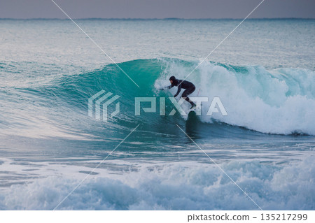 Surfer in winter wetsuit ride the blue waves in ocean. Surfer in winter wetsuit ride the blue waves in ocean. 135217299