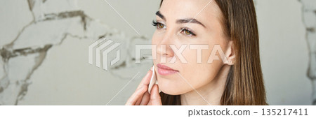 Young caucasian female with smooth skin applying skincare product to cheek Young caucasian female with smooth skin applying skincare product to cheek 135217411