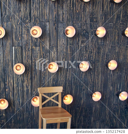 Rustic wooden wall with multiple lit light fixtures and single wooden chair 135217428