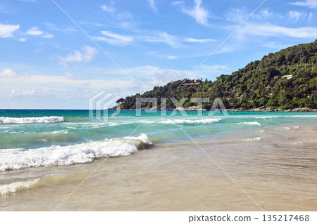 Sunny tropical beach with crystal clear waves and lush green hills on a clear 135217468