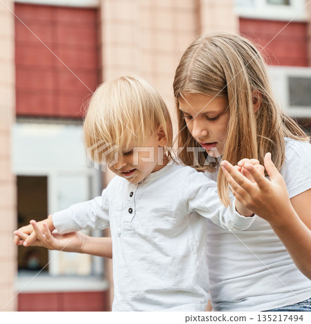 Caucasian female teen assisting young child with balance outside near red brick 135217494