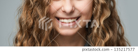 Smiling young caucasian female with curly brown hair and bright smile against Smiling young caucasian female with curly brown hair and bright smile against 135217577