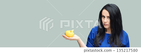 Young caucasian female holding yellow piggy bank against plain background 135217580