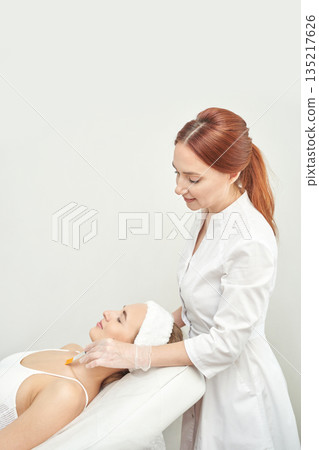 Caucasian female aesthetician applying facial treatment to relaxed young woman Caucasian female aesthetician applying facial treatment to relaxed young woman 135217626