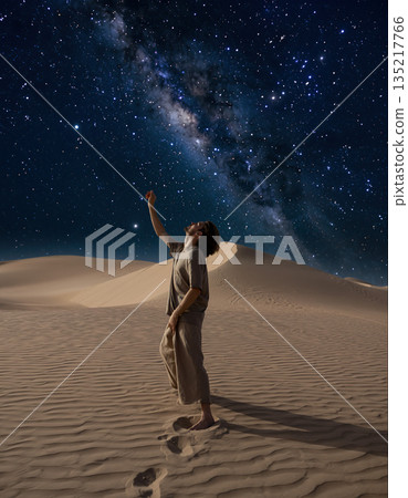 Person stands in desert at night looking up at the stars and the Milky Way shining brightly in the sky 135217766