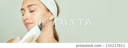 Young caucasian female using facial scrubber for skincare routine with closed 135217811