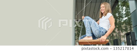 Caucasian young girl in casual outfit enjoying a swing in a modern outdoor 135217814