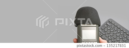 Hand holding audio recorder with microphone and wireless keyboard on gray Hand holding audio recorder with microphone and wireless keyboard on gray 135217831
