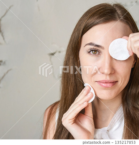 Young caucasian female cleansing face with cotton pads for skincare routine 135217853