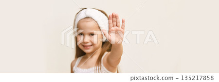 Smiling caucasian young girl with raised hand gesturing stop on a neutral Smiling caucasian young girl with raised hand gesturing stop on a neutral 135217858