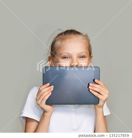 Caucasian young girl holding tablet and smiling in casual white shirt against 135217859