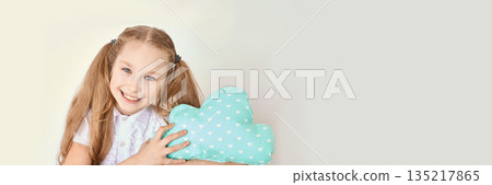 Smiling caucasian female child holding heart patterned cloud pillow against Smiling caucasian female child holding heart patterned cloud pillow against 135217865