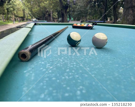 A pool table with balls and a cue in a city amusement park A pool table with balls and a cue in a city amusement park 135218230