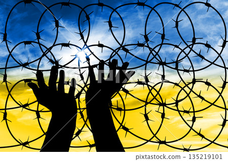 Silhouette of hands facing the sky against the background of a fence with barbed wire. Silhouette of hands facing the sky against the background of a fence with barbed wire. 135219101