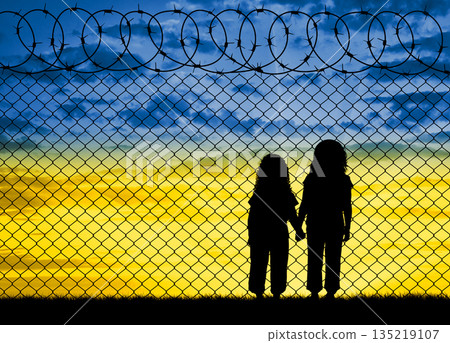 Ukrainian refugees - children, at the barbed wire fence against the sky in the form of the flag of Ukraine Ukrainian refugees - children, at the barbed wire fence against the sky in the form of the flag of Ukraine 135219107