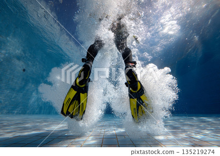 Diver in black wetsuit with yellow fins creating splashes in a clear swimming pool environment Diver in black wetsuit with yellow fins creating splashes in a clear swimming pool environment 135219274