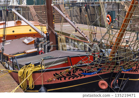 Close-up of two docked Dutch boats vibrant hulls with nautical gear, brick harbor steps, and metal railing showcase maritime craftsmanship and functional harbor design. 135219471