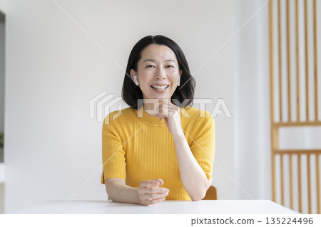 A woman in her 50s wearing earphones and talking while looking at the camera 135224496