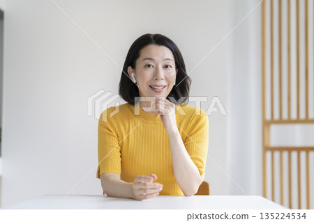 一位五十多歲的女子戴著耳機,一邊看著鏡頭一邊說話。 一位五十多歲的女子戴著耳機,一邊看著鏡頭一邊說話。 135224534