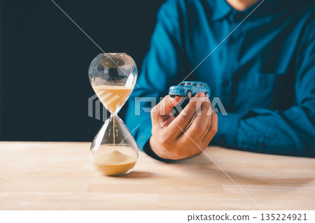 Individual holds car, hourglass shows time passing, symbolizing finance, loan, and saving money, crucial for understanding car cost, insurance, and depreciation for business 135224921