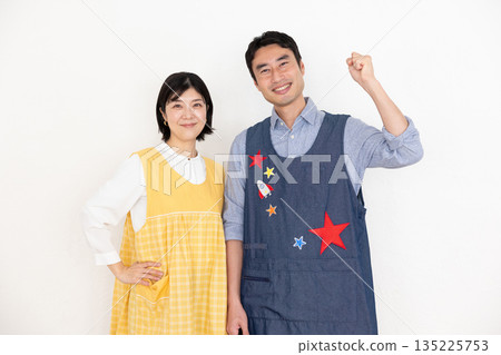 Smiling male and female nursery teachers wearing aprons smiling Smiling male and female nursery teachers wearing aprons smiling 135225753
