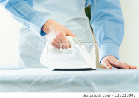 Hands of a woman ironing a dress shirt 135226043