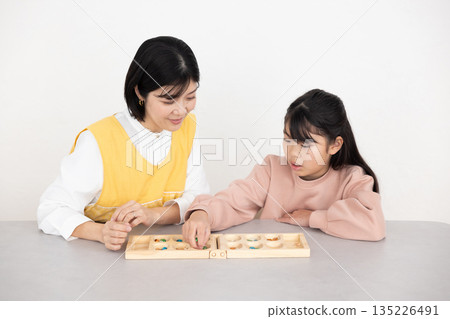 Elementary school girl and middle-aged woman wearing apron enjoying Mancala 135226491