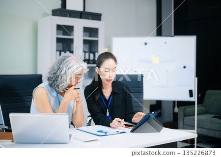 Asian senior and middle aged businesswomen working together in office. Professional teamwork, mentorship, business collaboration Asian senior and middle aged businesswomen working together in office. Professional teamwork, mentorship, business collaboration 135226873