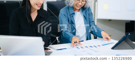 Asian senior and middle aged businesswomen working together in office, using smartphone and tablet Asian senior and middle aged businesswomen working together in office, using smartphone and tablet 135226980