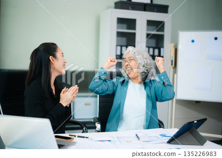 Asian senior and middle aged businesswomen reviewing documents and reports in office. Professional teamwork, mentorship, business collaboration Asian senior and middle aged businesswomen reviewing documents and reports in office. Professional teamwork, mentorship, business collaboration 135226983